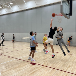 Students playing in an intramural basketball game. One student attempts a layup as others defend.